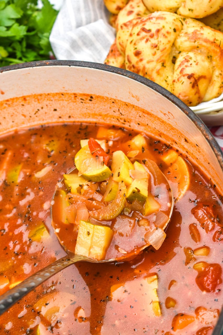 a silver ladle scooping italian summer soup out of a dutch oven