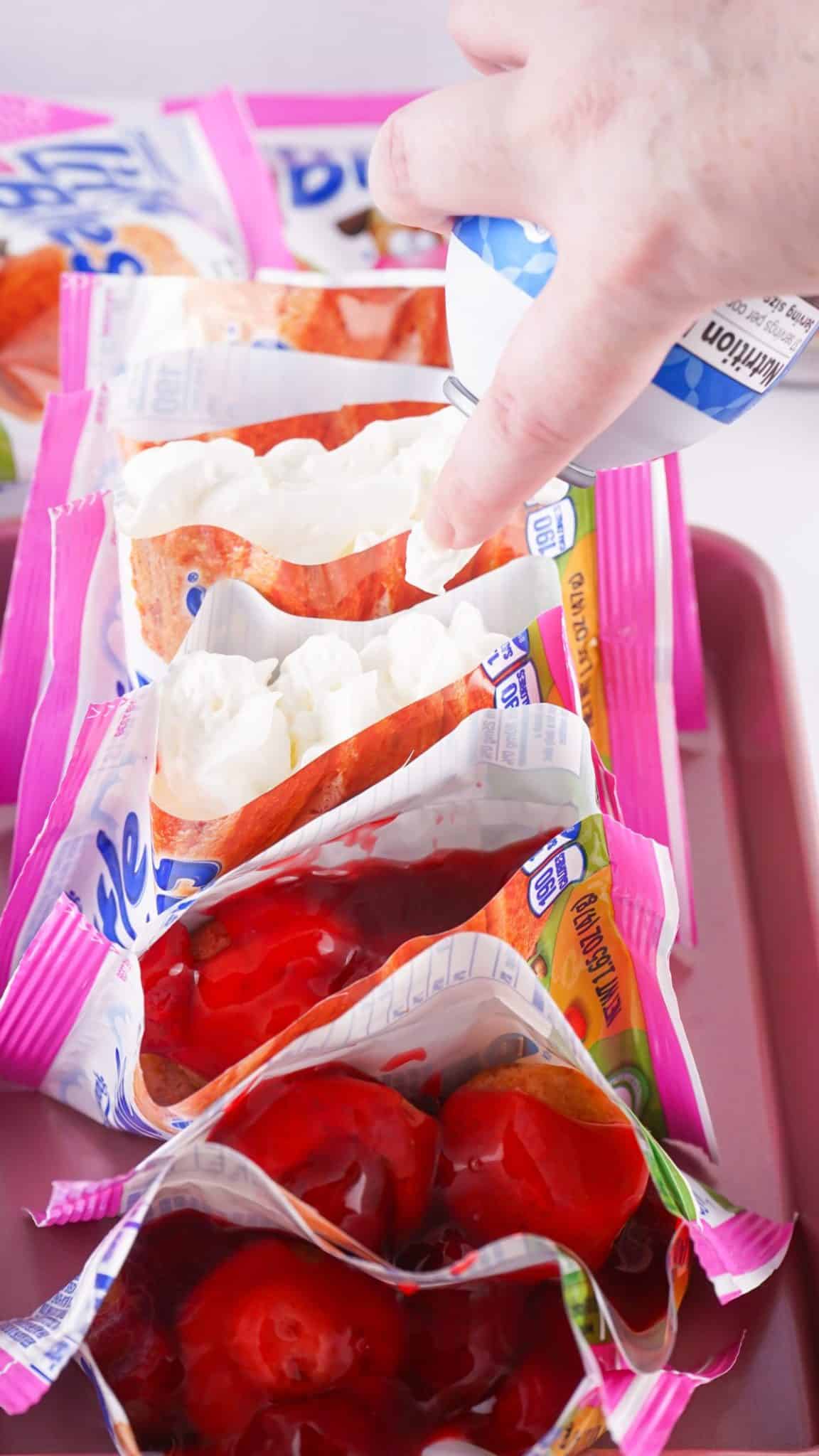 whipped cream being piped onto strawberry sauce topped mini muffins in their packages