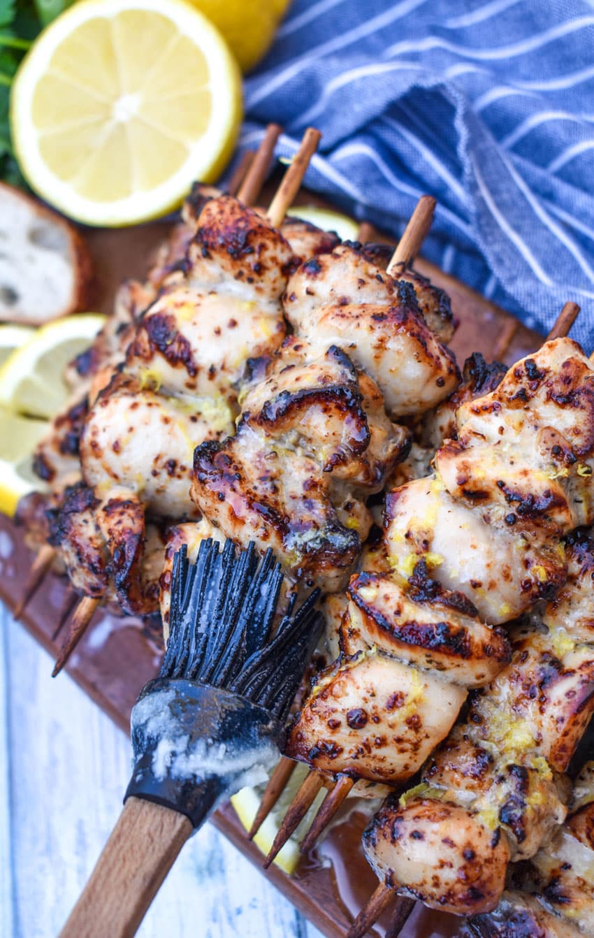 a silicone brush brushing lemon butter over chicken skewers