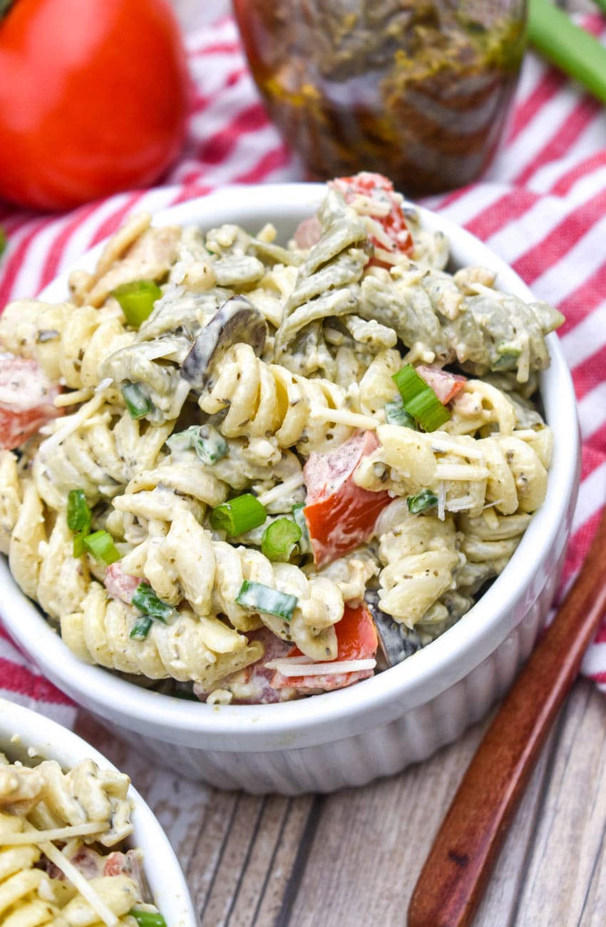 creamy caesar pesto pasta salad in two white ramekins with wooden spoons on the side