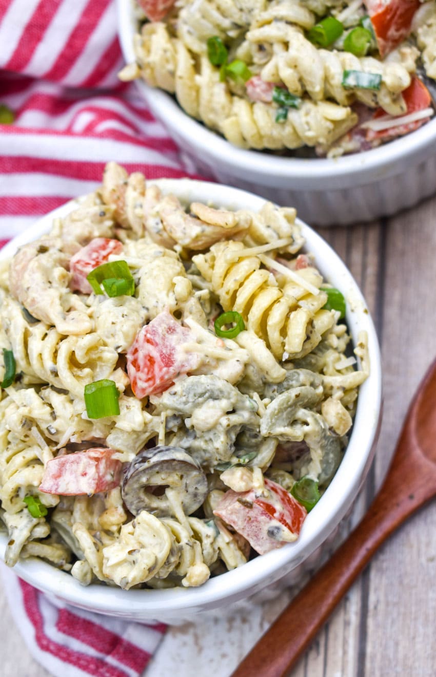 creamy caesar pesto pasta salad in two white ramekins with wooden spoons on the side