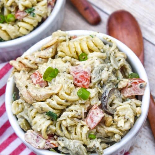 creamy caesar pesto pasta salad in two white ramekins with wooden spoons on the side