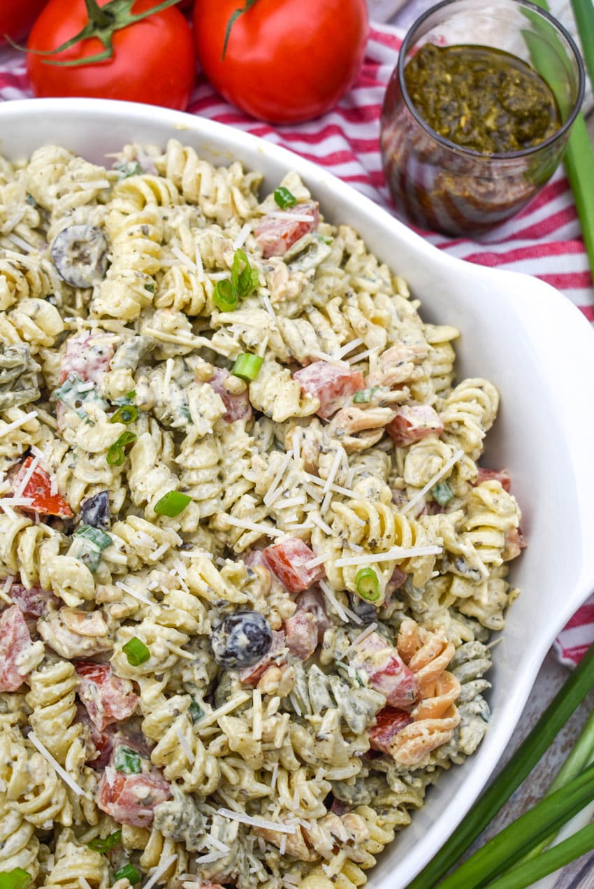 creamy caesar pesto pasta salad in a large white serving bowl
