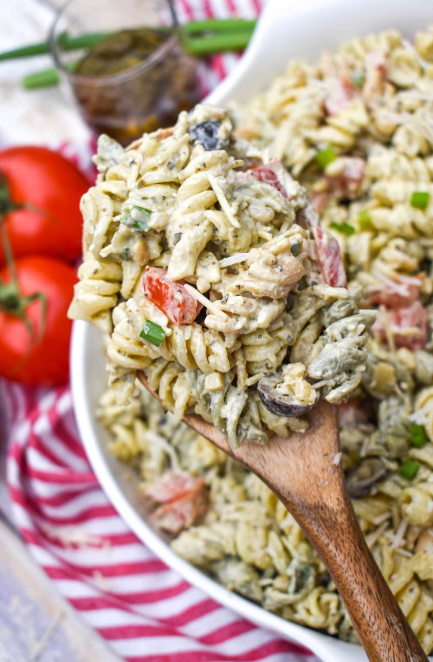 a wooden spoon holding up a scoop of creamy caesar pesto pasta salad