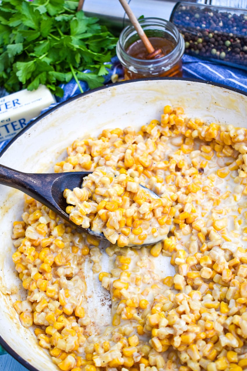 a wooden spoon scooping creamy honey butter canned corn out of a cast iron skillet