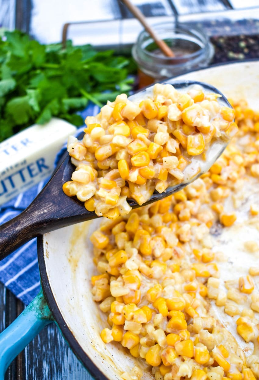 a wooden spoon holding up a scoop of creamy honey butter canned corn