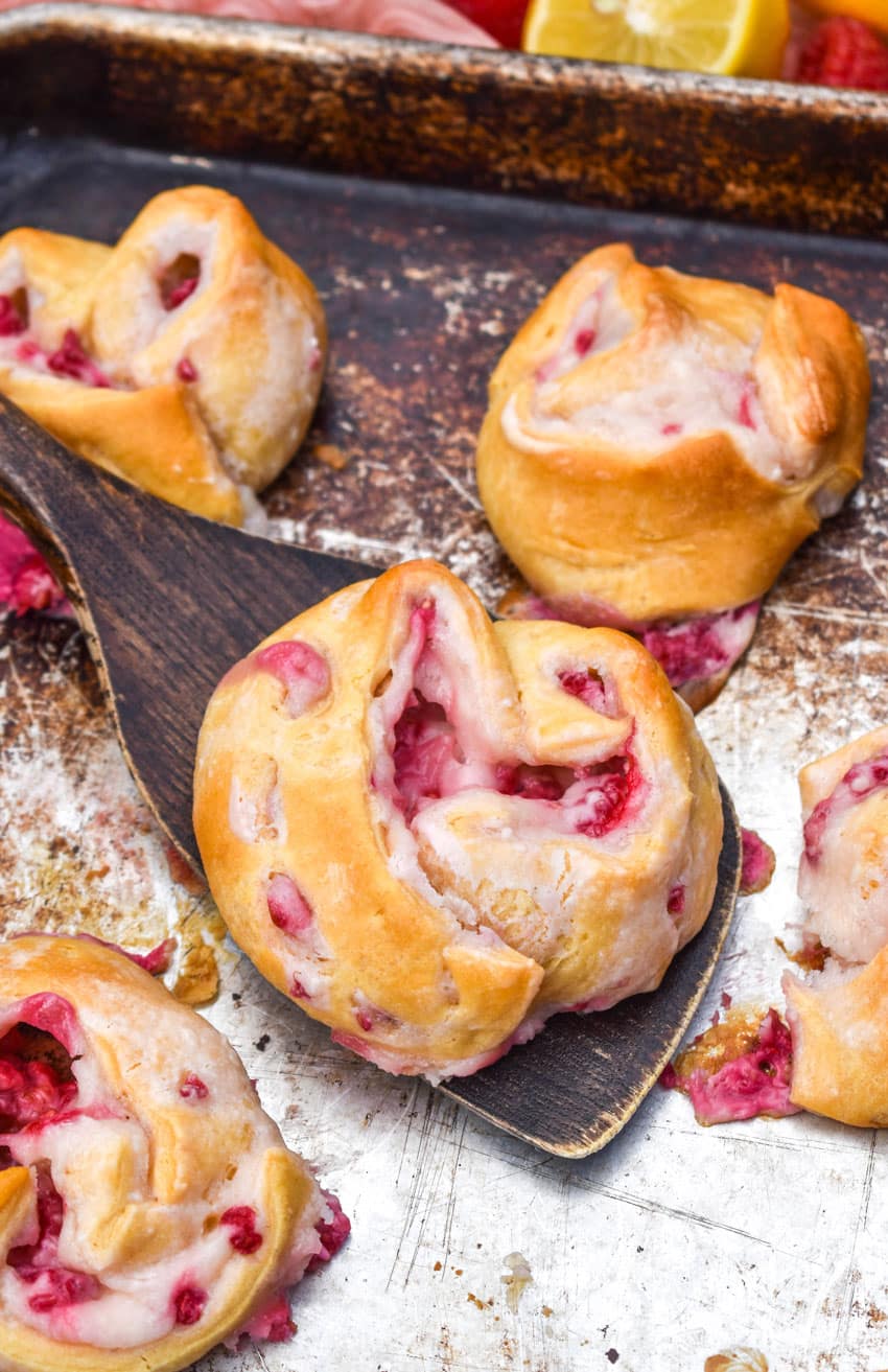 a wooden spatula scooping a raspberry lemon danish off of a metal baking sheet