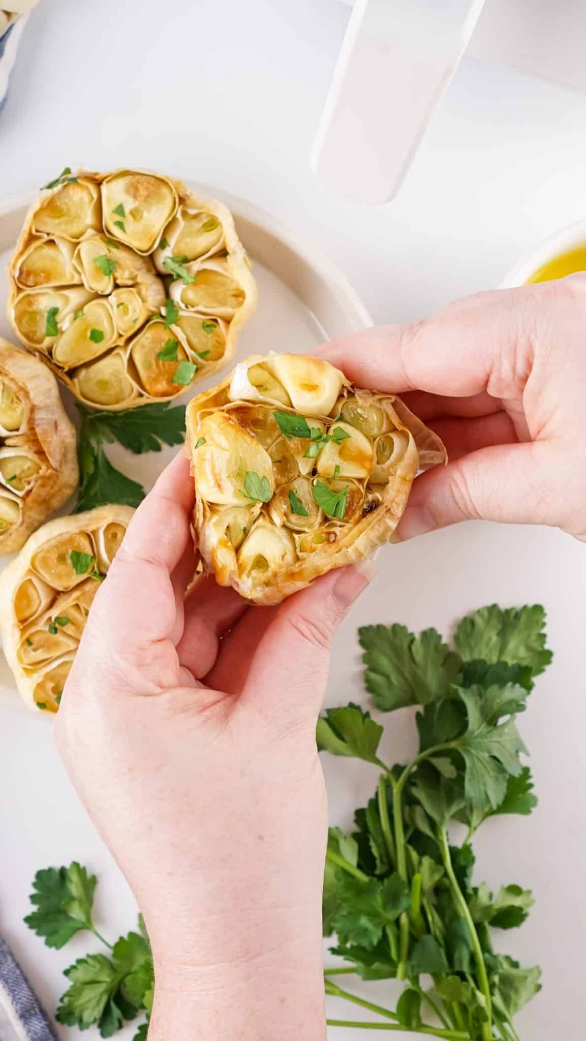 a hand squeezing roasted garlic cloves out of a bulb