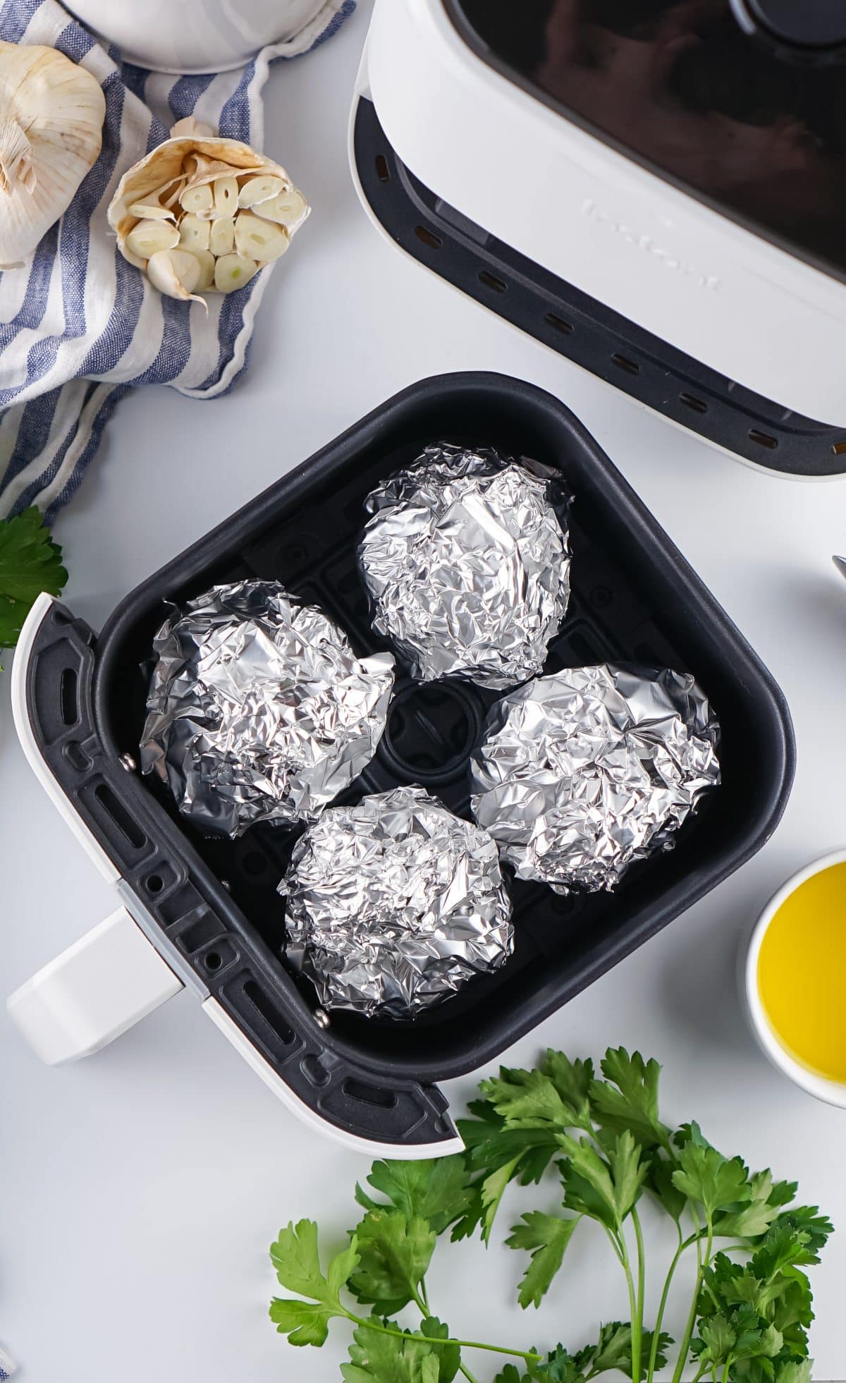 4 oiled garlic bulbs wrapped in aluminum foil in the basket of an air fryer