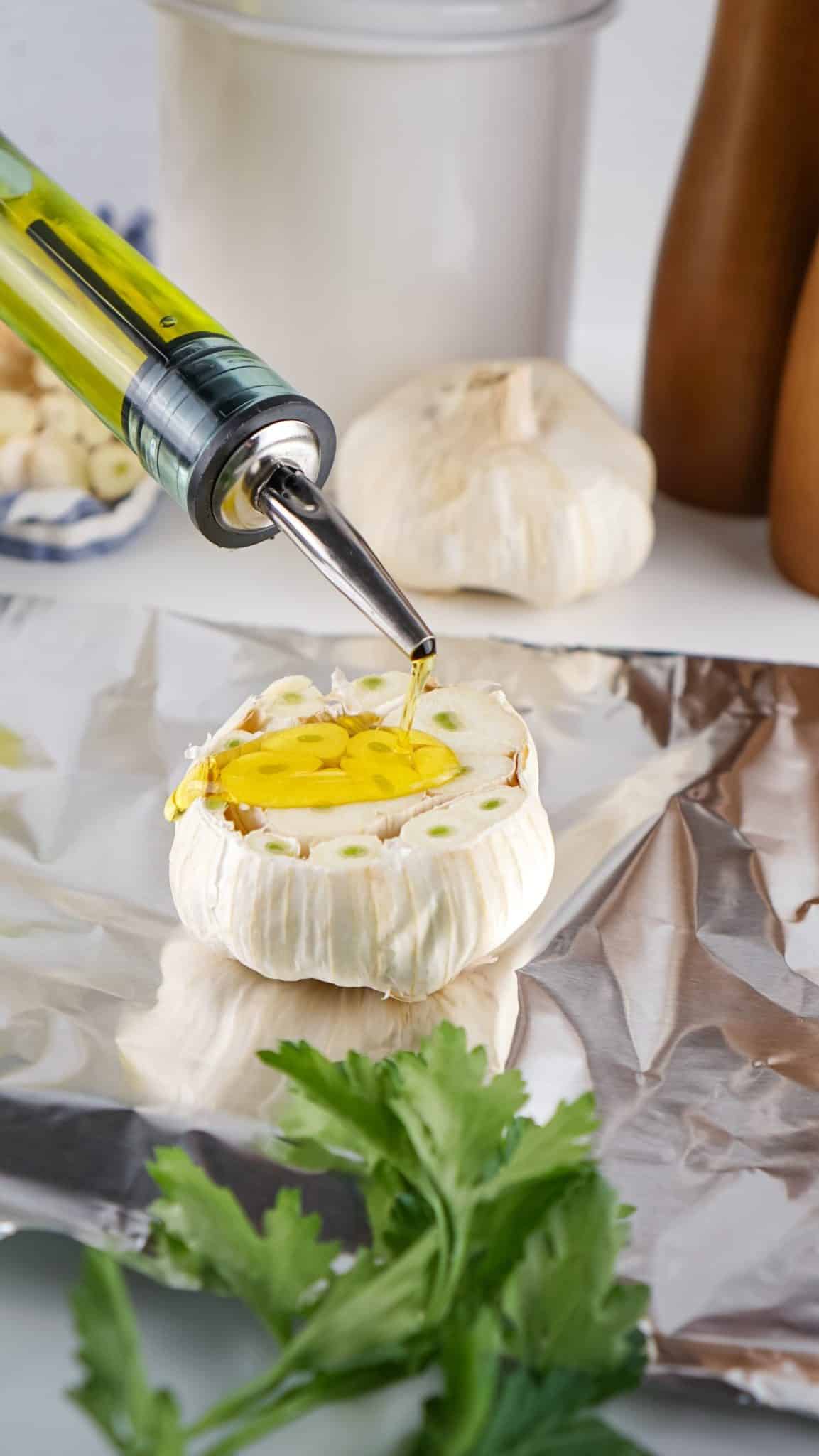 olive oil being poured onto a halved garlic bulb on a sheet of aluminum foil