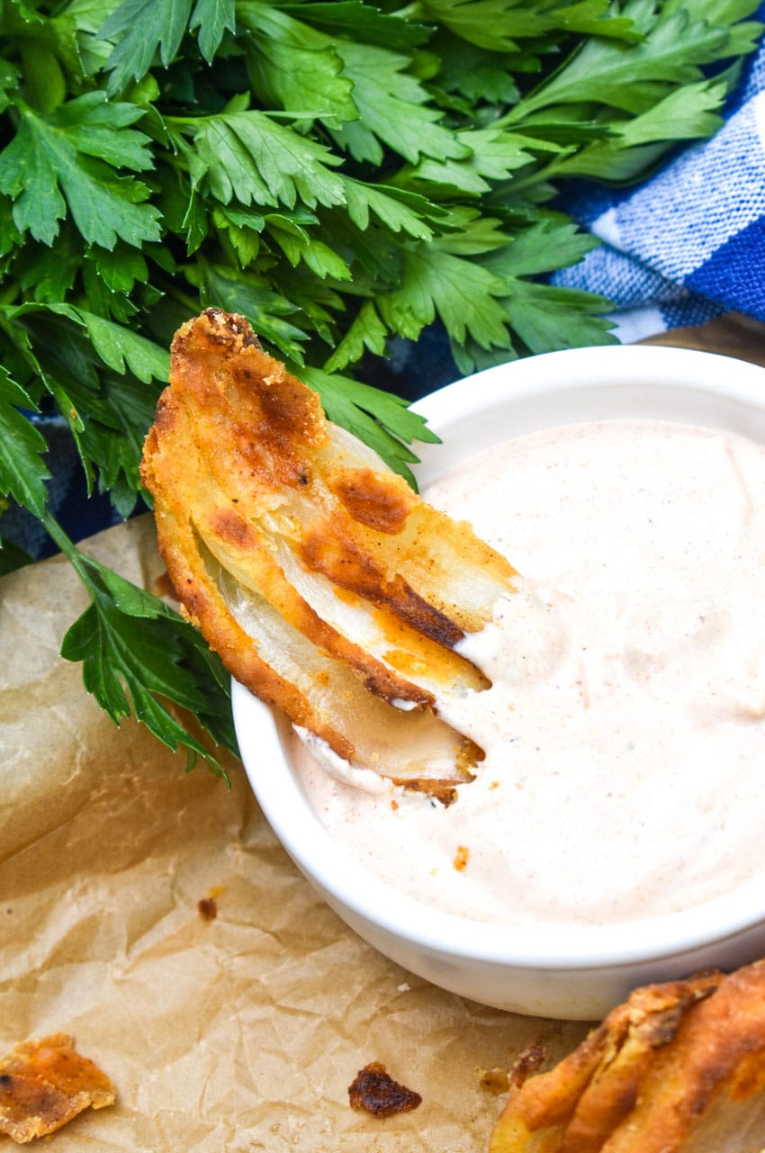 a close up of bloomin onion petals resting on the edge of a bowl filled with dipping sauce