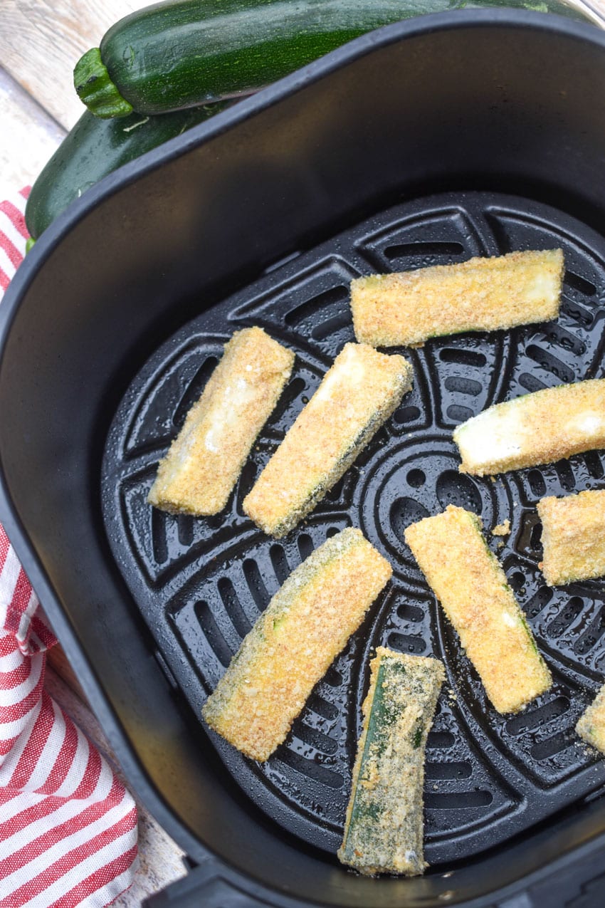 breaded sticks of zucchini in the basket of an air fryer