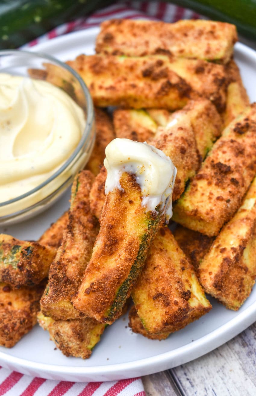 air fryer zucchini fries on a white serving plate with a small bowl of aioli dip on the side