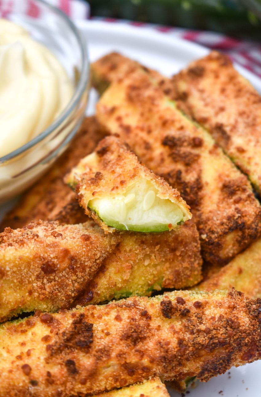 air fryer zucchini fries on a white serving plate with a small bowl of aioli dip on the side