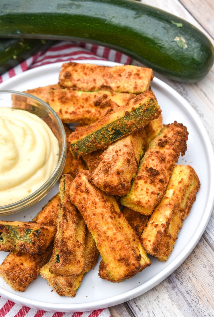 air fryer zucchini fries on a white serving plate with a small bowl of aioli dip on the side