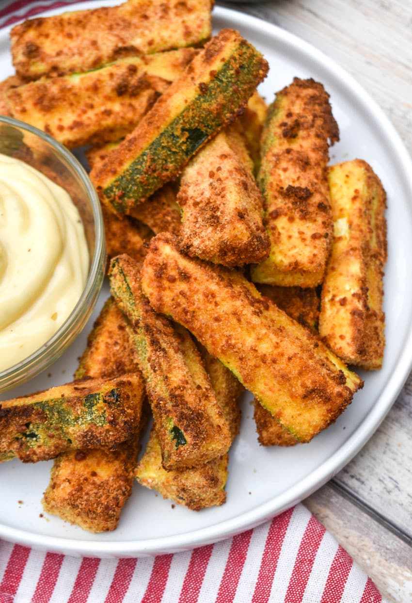 air fryer zucchini fries on a white serving plate with a small bowl of aioli dip on the side