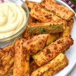 air fryer zucchini fries on a white serving plate with a small bowl of aioli dip on the side