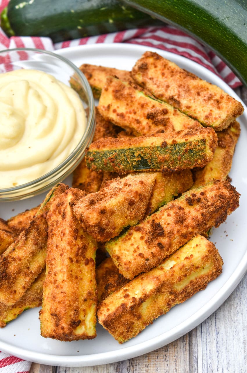 air fryer zucchini fries on a white serving plate with a small bowl of aioli dip on the side