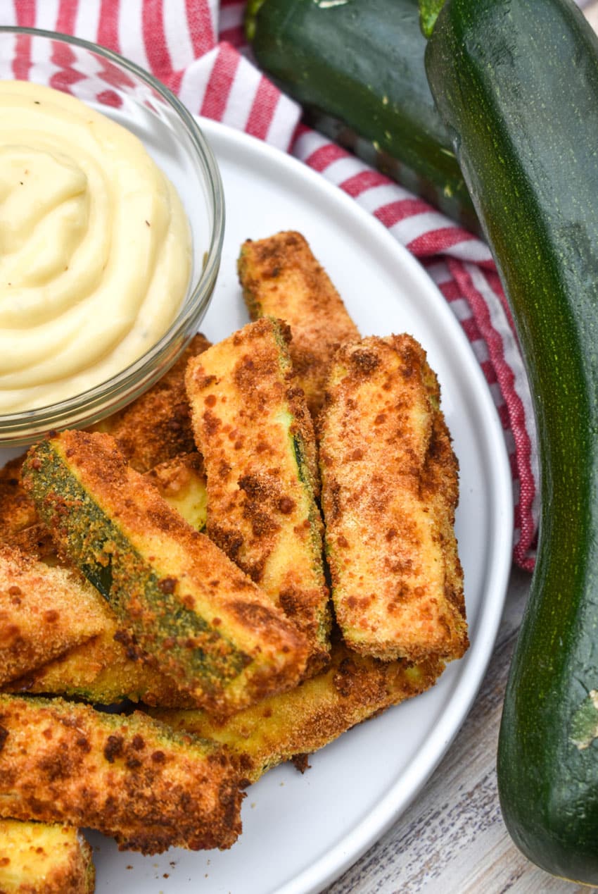 air fryer zucchini fries on a white serving plate with a small bowl of aioli dip on the side