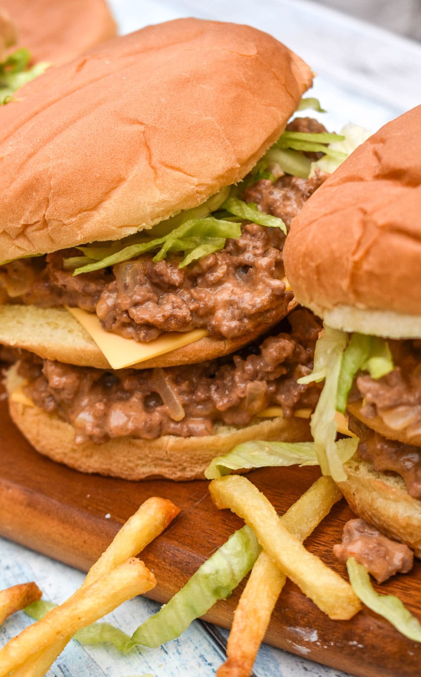 big mac sloppy joes on a wooden cutting board surrounded by crispy french fries