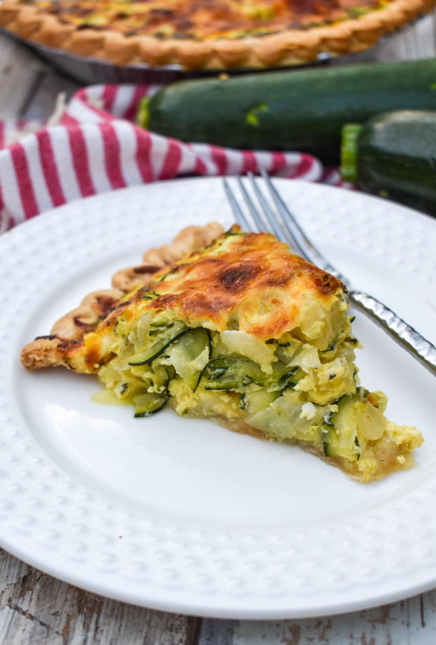 a slice of cheesy zucchini quiche on a small white plate with a silver fork resting on the side