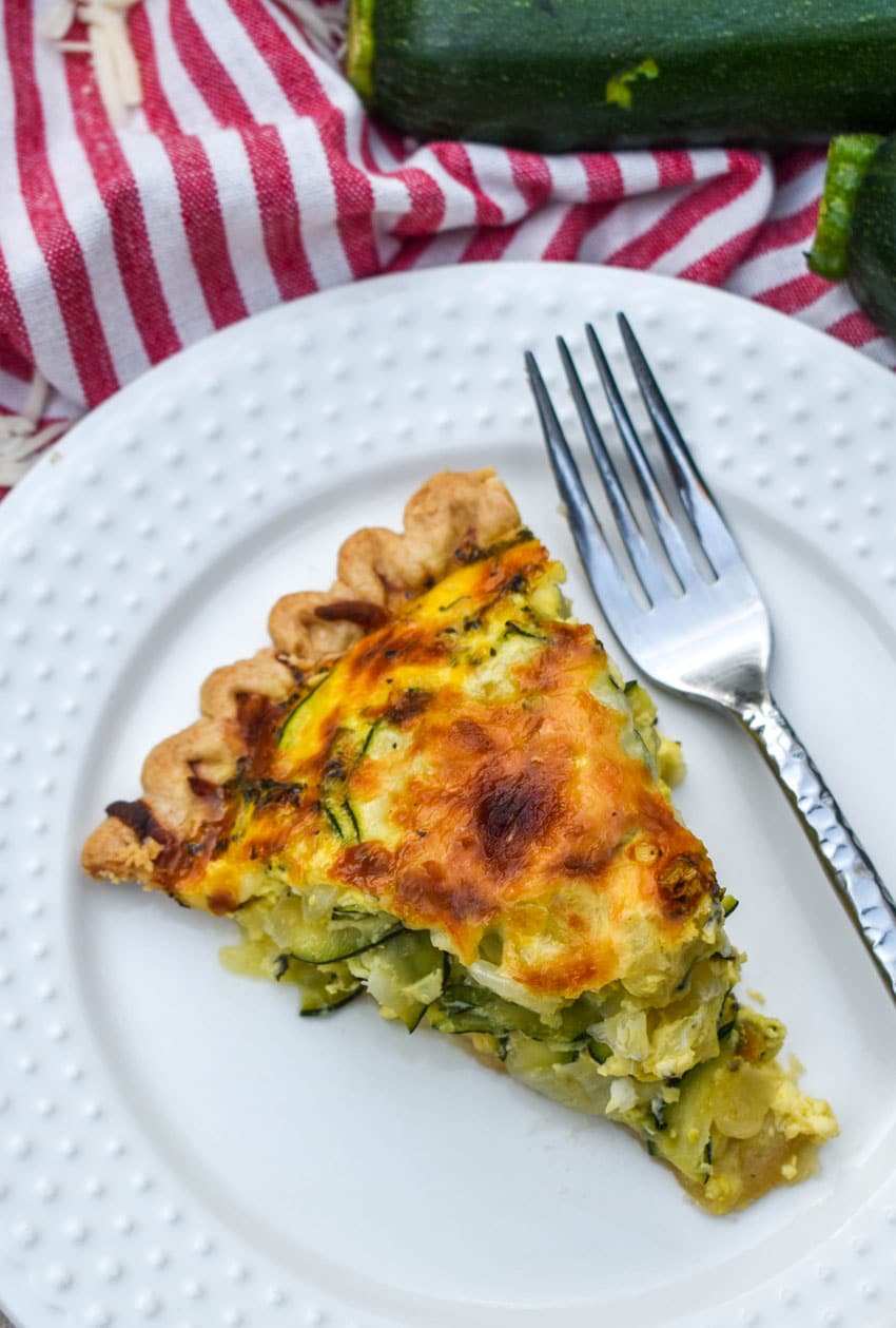 a slice of cheesy zucchini quiche on a small white plate with a silver fork resting on the side
