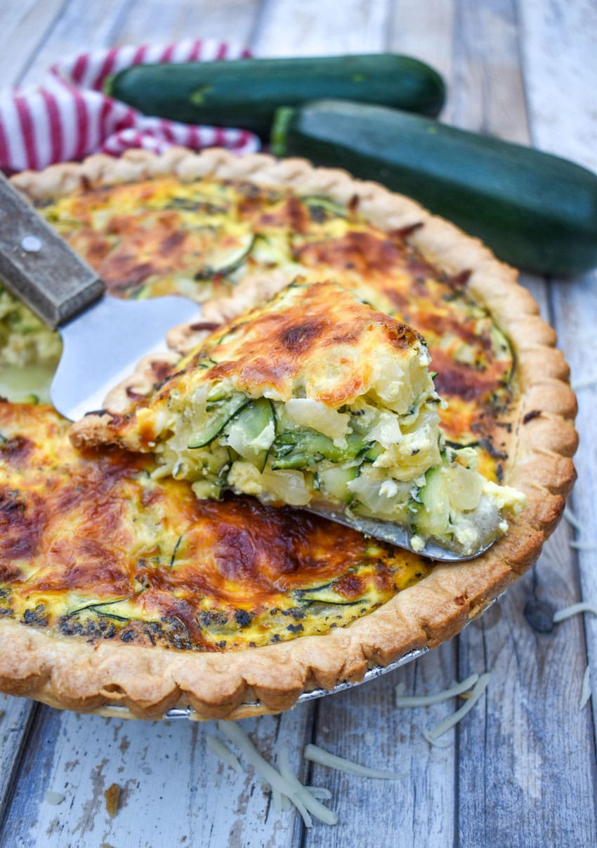a wooden handled server resting with a slice of zucchini quiche on top of a zucchini quiche