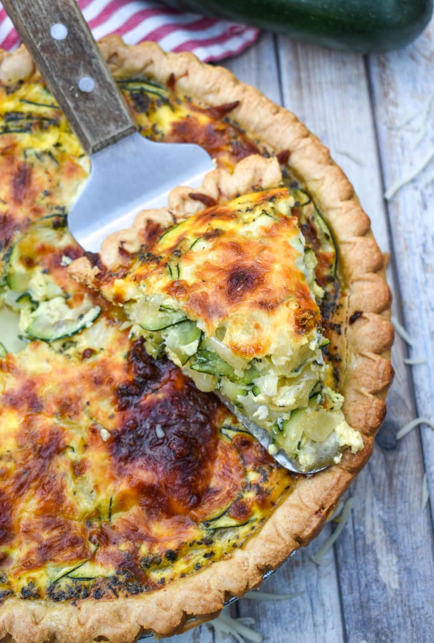 a wooden handled server resting with a slice of zucchini quiche on top of a zucchini quiche