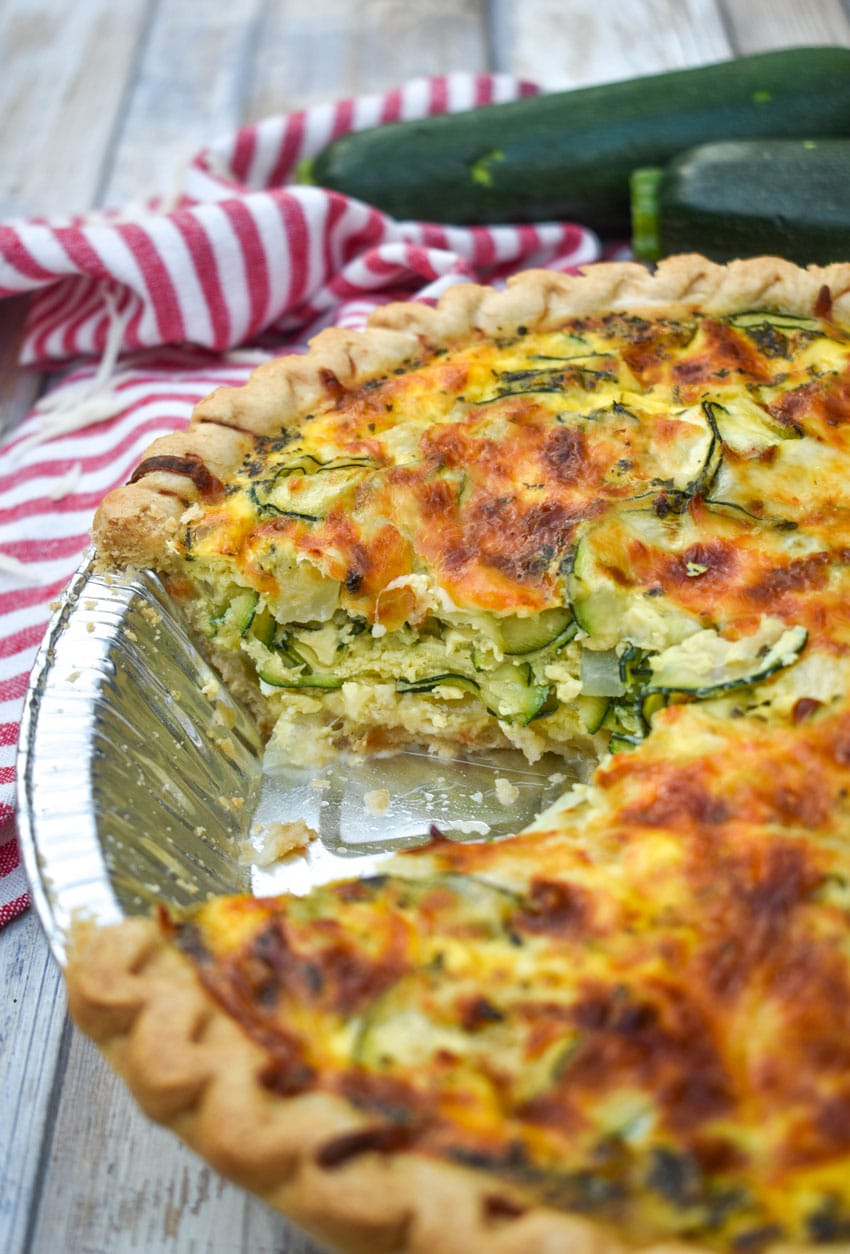 a zucchini quiche with a slice removed in a tin foil pie pan