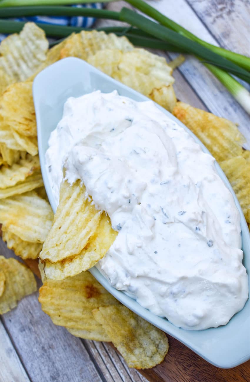 a potato chip dipped in homemade dean's french onion dip in a small gray serving bowl