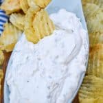 a potato chip dipped in homemade dean's french onion dip in a small gray serving bowl