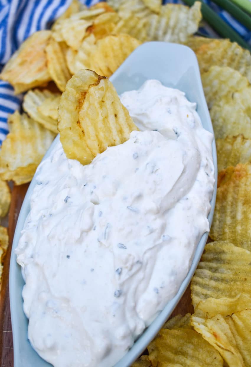 a potato chip dipped in homemade dean's french onion dip in a small gray serving bowl