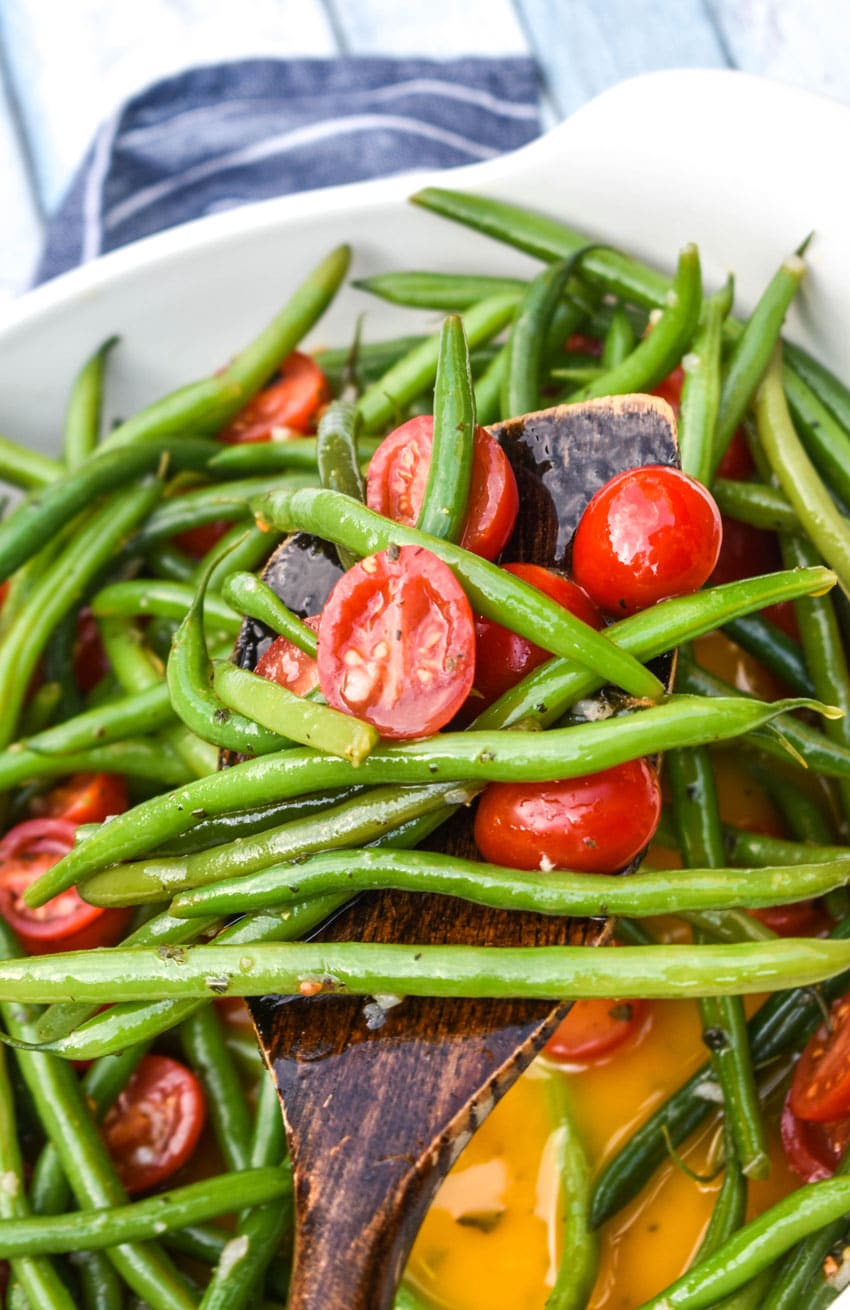 a wooden spatula holding up a scoop of green bean and tomato salad