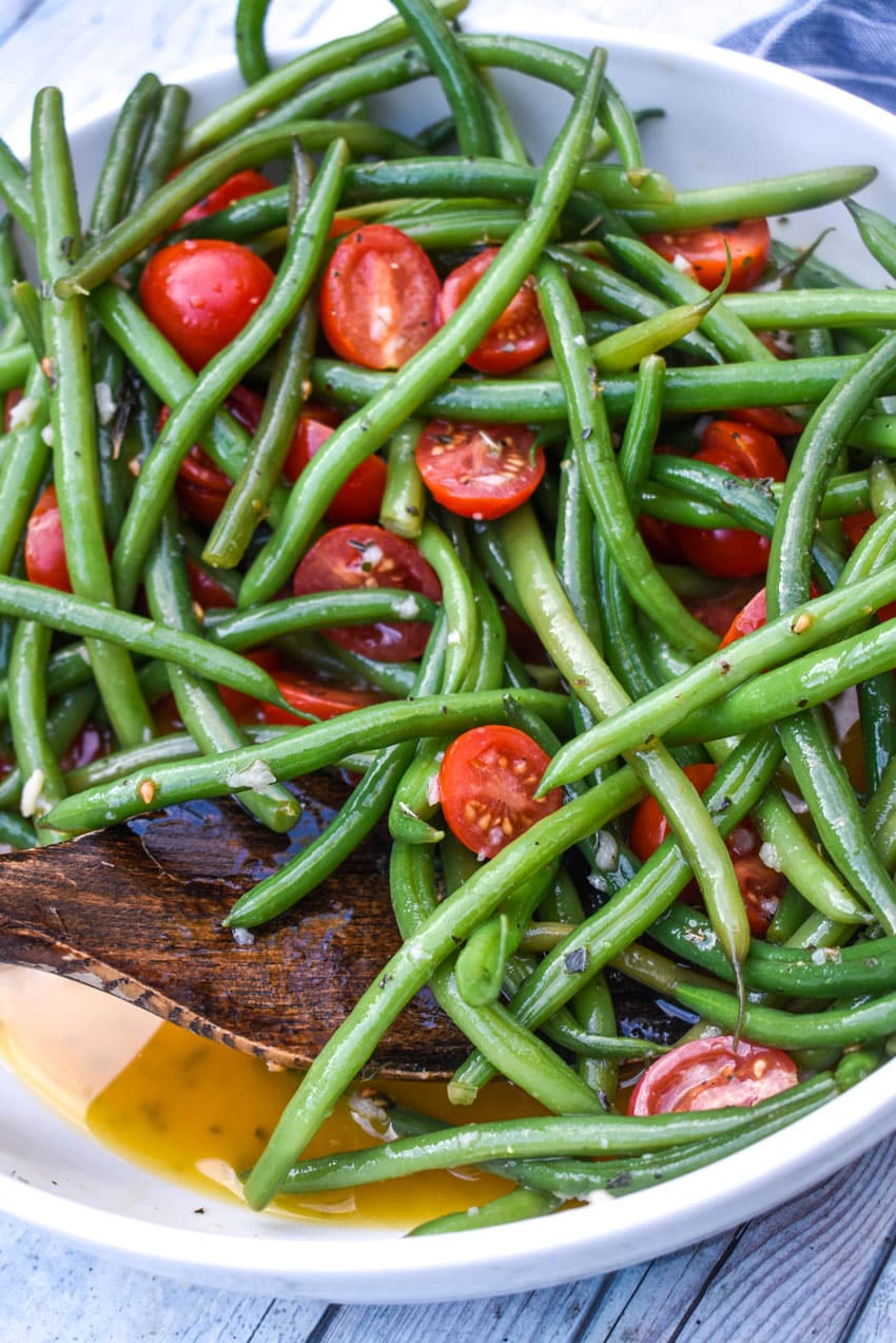 a wooden spatula scooping green bean and tomato salad out of a white serving bowl