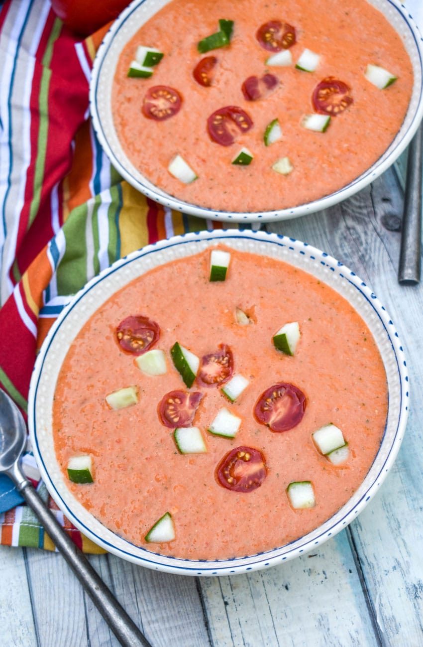 homemade gazpacho topped with diced cucumber and tomato in two white bowls