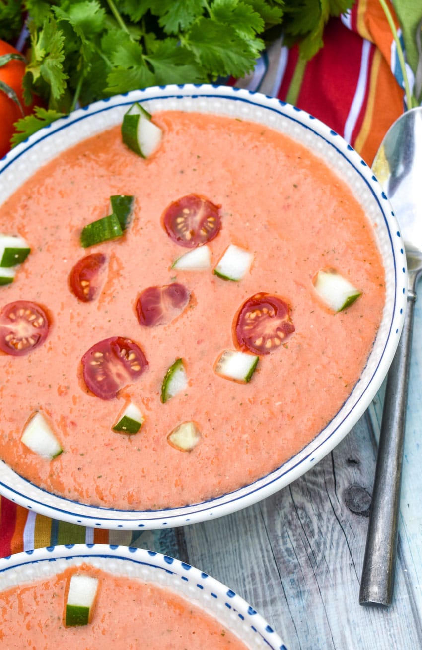 homemade gazpacho topped with diced cucumber and tomato in two white bowls