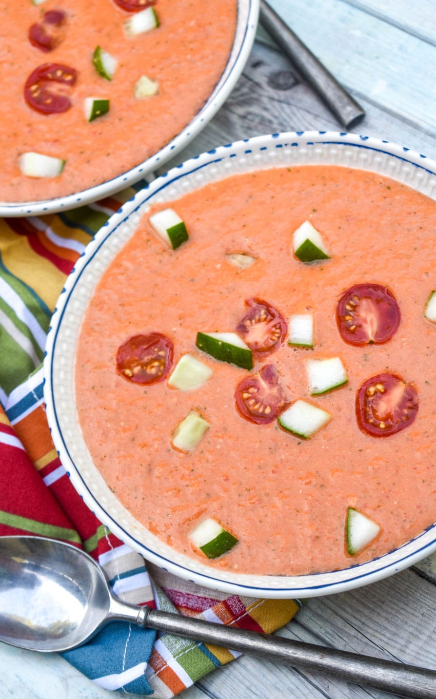 homemade gazpacho topped with diced cucumber and tomato in two white bowls