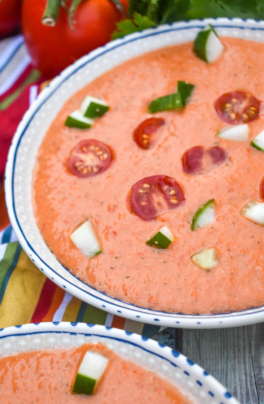 homemade gazpacho topped with diced cucumber and tomato in two white bowls