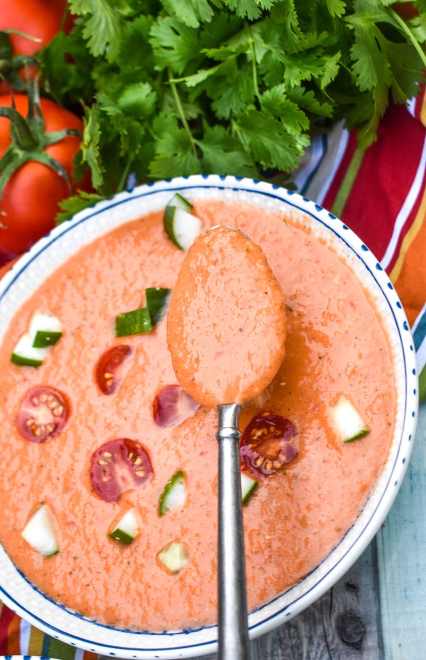 a silver spoon ladling a scoop of homemade gazpacho out of a white bowl