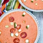 homemade gazpacho topped with diced cucumber and tomato in two white bowls