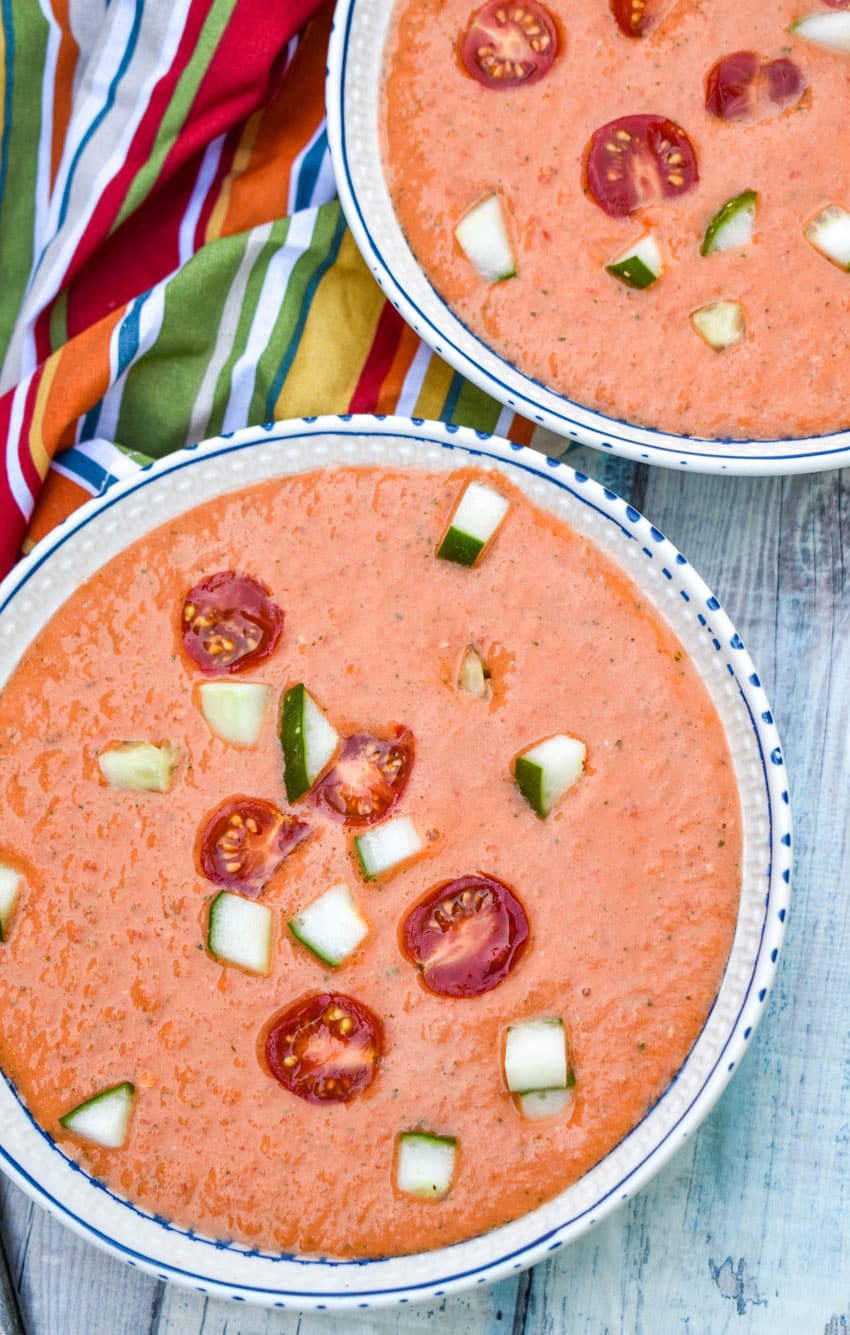 homemade gazpacho topped with diced cucumber and tomato in two white bowls