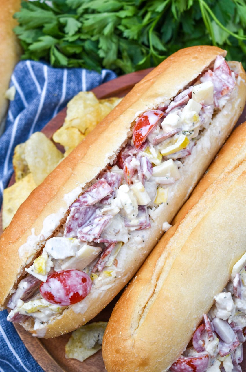 italian grinder chicken salad on two hoagie buns resting on a wooden cutting board