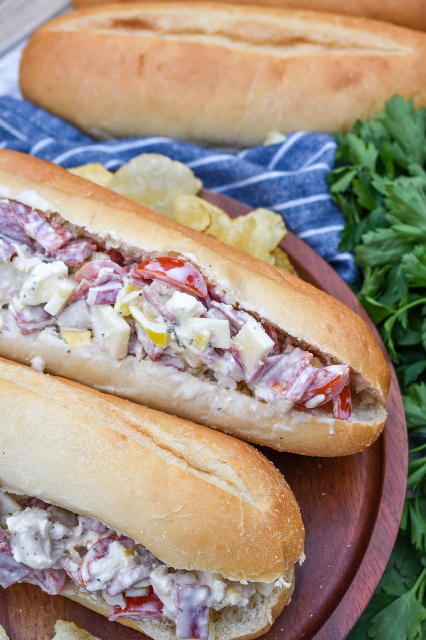 italian grinder chicken salad on two hoagie buns resting on a wooden cutting board