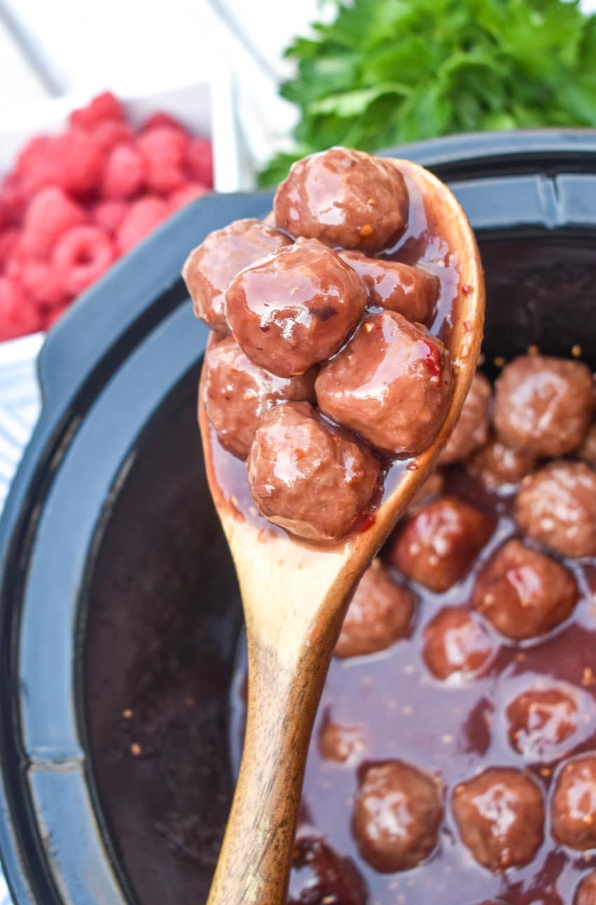 a wooden spoon holding up a scoop of the best slow cooker party meatballs