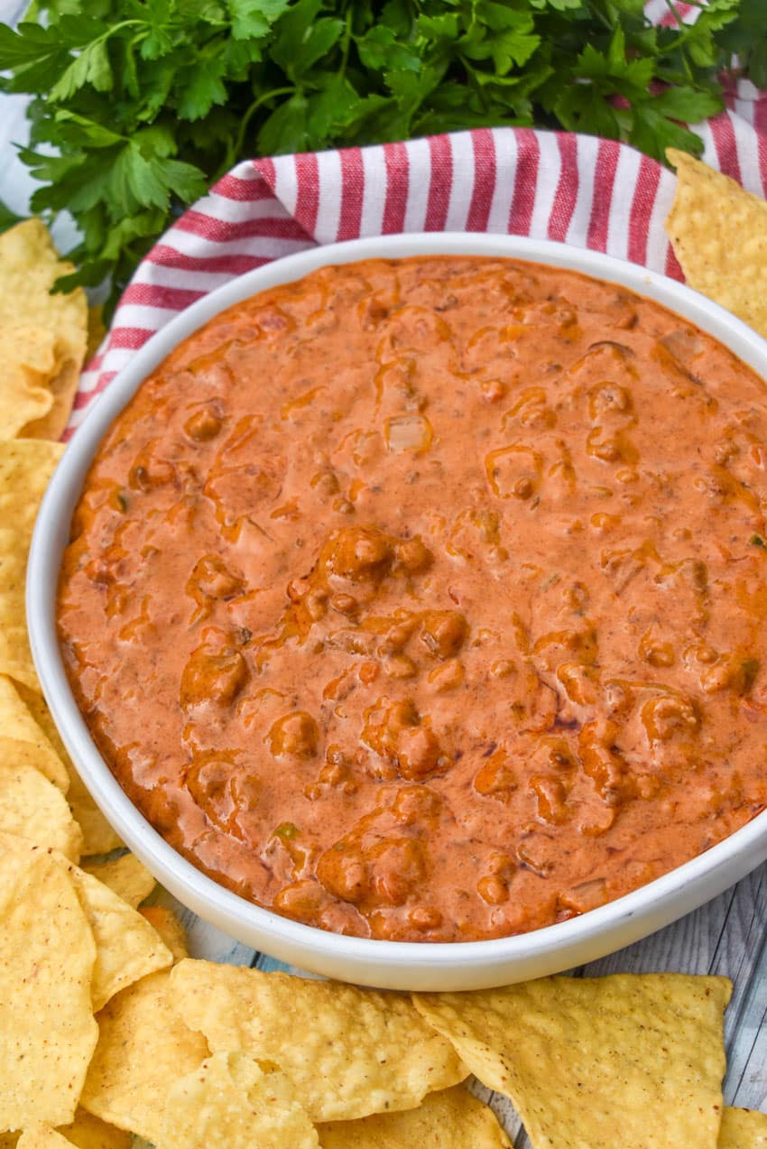 CHILI CHEESE DIP IN A SHALLOW WHITE SERVING BOWL SURROUNDED BY TORTILLA CHIPS