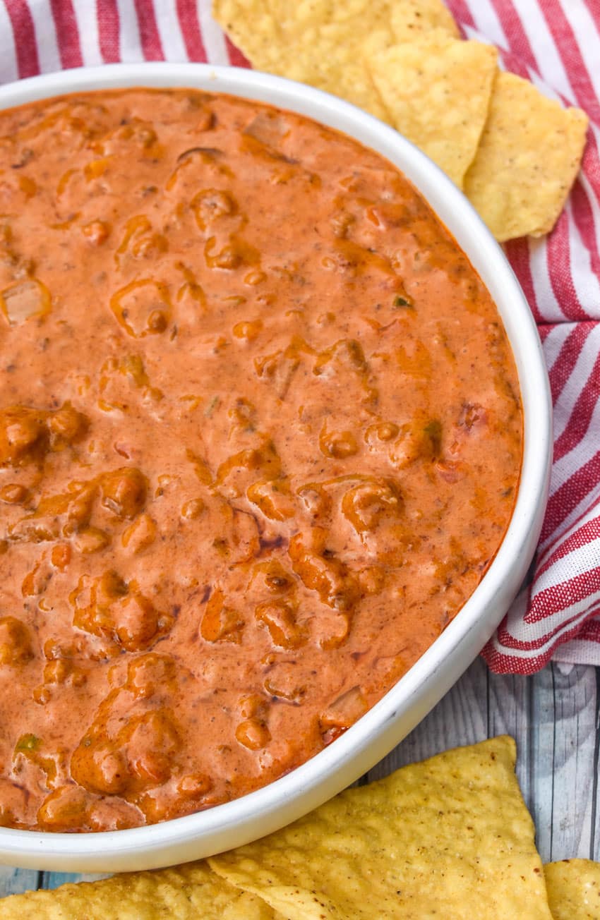 CHILI CHEESE DIP IN A SHALLOW WHITE SERVING BOWL SURROUNDED BY TORTILLA CHIPS