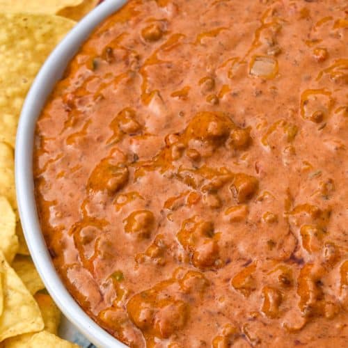 CHILI CHEESE DIP IN A SHALLOW WHITE SERVING BOWL SURROUNDED BY TORTILLA CHIPS