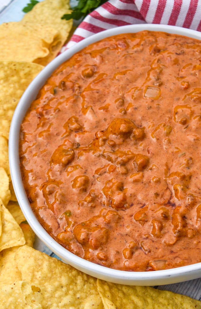 CHILI CHEESE DIP IN A SHALLOW WHITE SERVING BOWL SURROUNDED BY TORTILLA CHIPS
