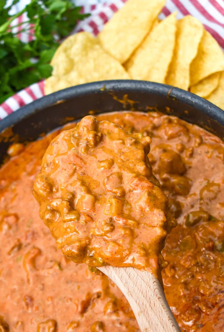 A WOODEN SPOON HOLDING UP A SCOOP OF THE BEST HOMEMADE CHILI CHEESE DIP