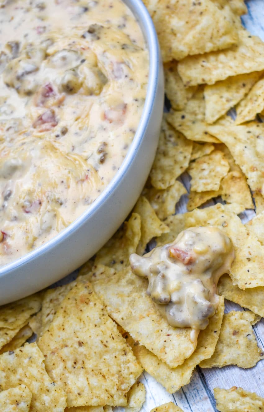 a tortilla chip topped with creamy slow cooker queso dip resting on a bed of other tortilla chips